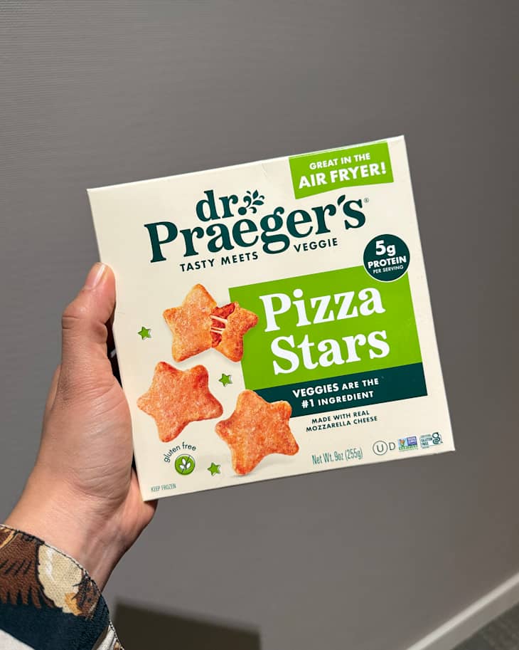 Hand holding a box of Dr. Praeger's Pizza Stars, featuring star-shaped veggie snacks with a green and white design.