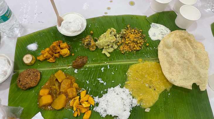 A traditional meal served on a banana leaf featuring rice, various curries, a papadum, and yogurt.