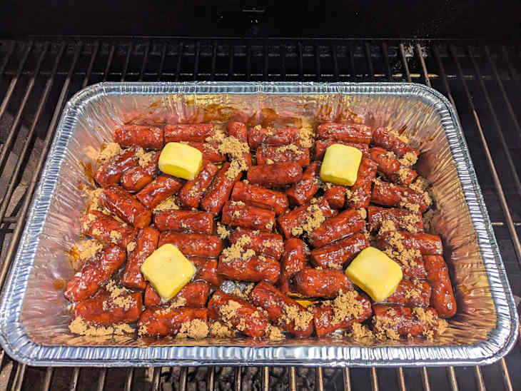 burnt hot dog ends with pats of butter in aluminum baking pan in oven