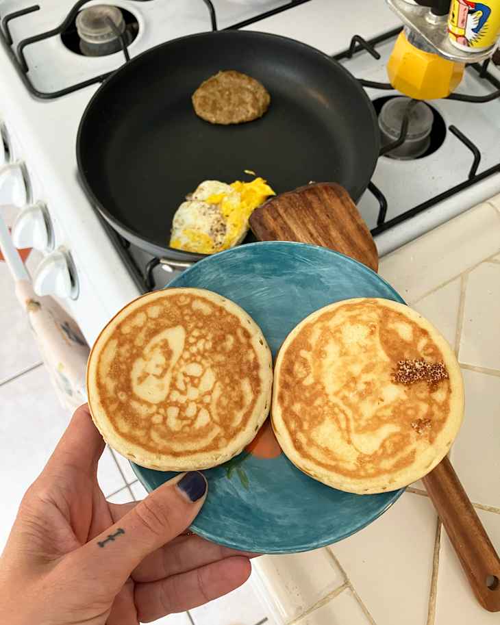 Trader Joe’s Dutch Griddle Cakes o plate with eggs and sausage cooking in background