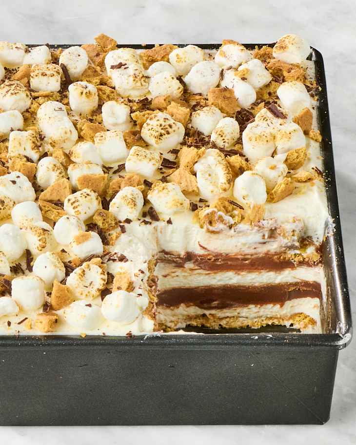 Layers of S’mores Icebox Cake with toasted marshmallows, graham cracker pieces, and chocolate filling in a baking dish.