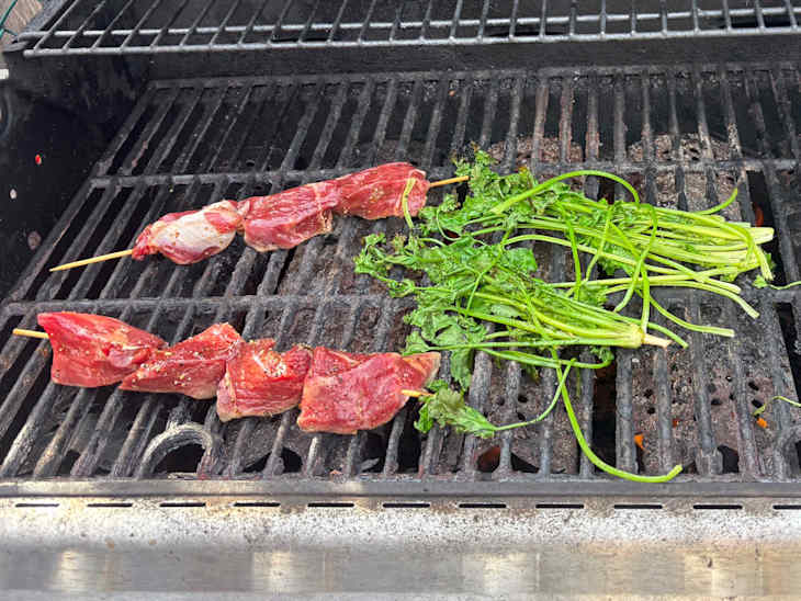 Skewers of marinated meat and fresh herbs grilling on a barbecue.