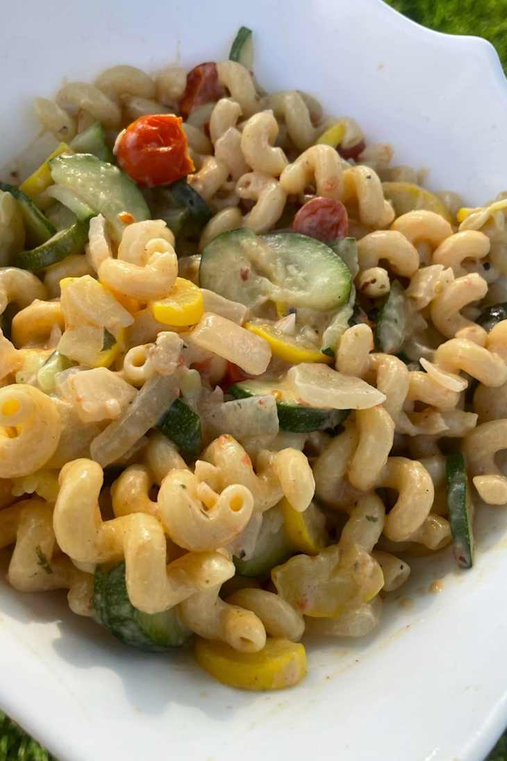 Creamy pasta salad with elbow macaroni, zucchini, yellow squash, cherry tomatoes, and herbs in a white bowl.