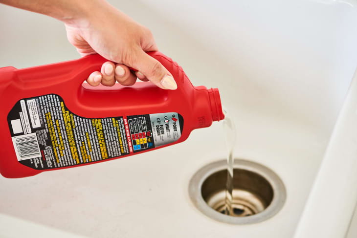 Hand pouring liquid drain cleaner from a red bottle into a sink drain.