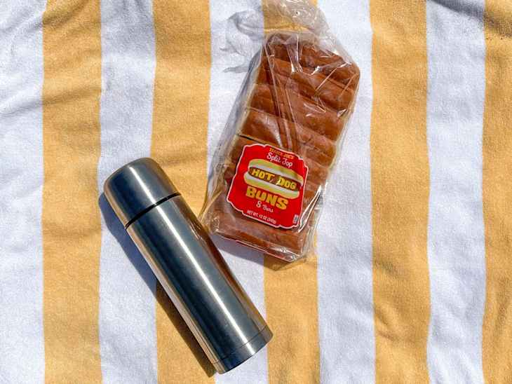 Thermos full of hot dog water, buns on a beach.