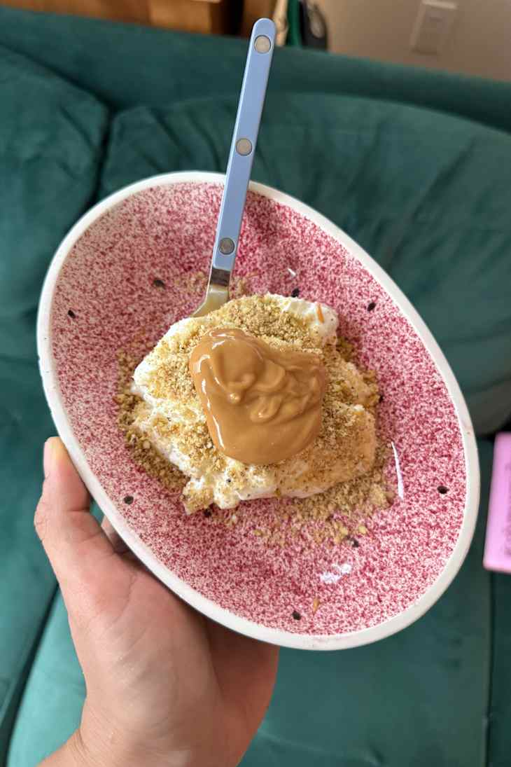 A hand holding a bowl with yogurt topped with peanut butter and crushed crackers.