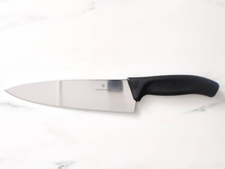 Chef's knife with a sleek stainless steel blade and a black handle, resting on a marble surface.