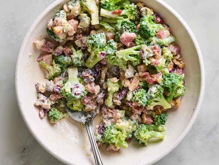 Bowl of broccoli salad with bacon, walnuts, and creamy dressing, mixed together with a spoon.