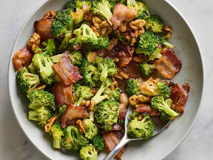 A bowl of sautéed broccoli with crispy bacon and walnuts, garnished with diced onions.