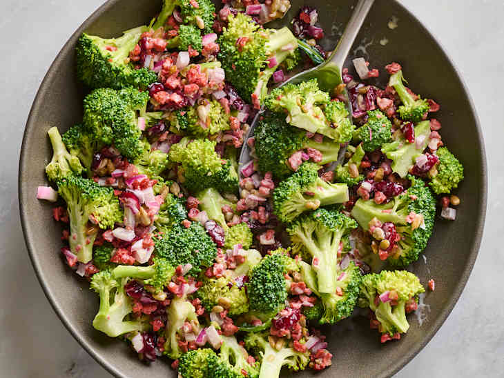 Chopped broccoli salad with red onion, cranberries, and sunflower seeds in a dark bowl.