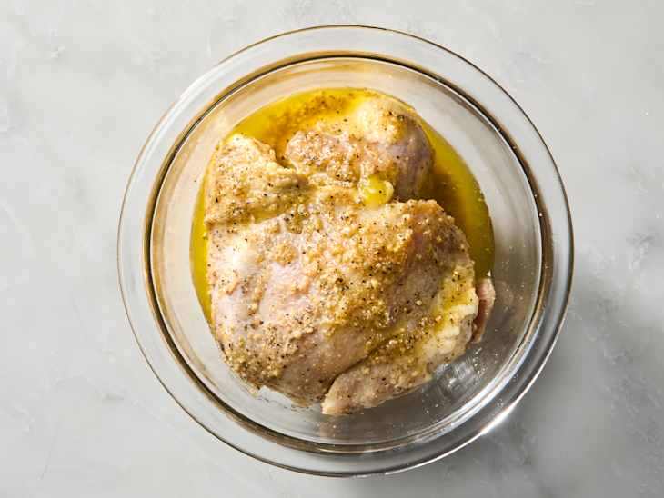 Marinated chicken thighs in a glass bowl with olive oil and spices.