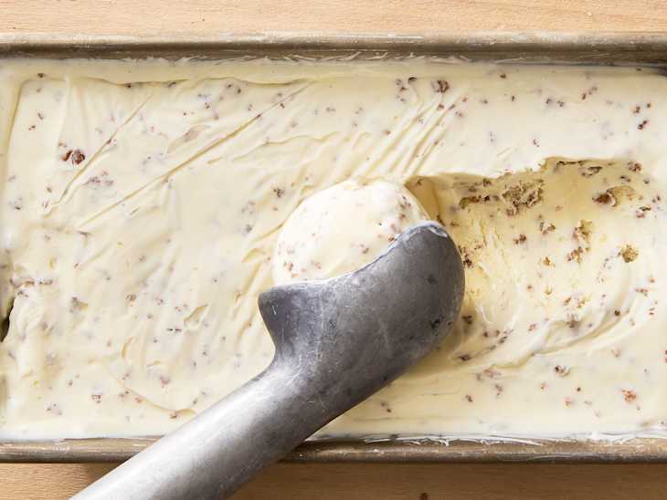 Creamy ice cream with nut pieces in a metal container, with a scoop partially removed.
