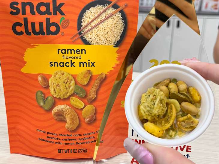 A hand holding a small white bowl filled with ramen-flavored snack mix, next to a colorful snack bag.