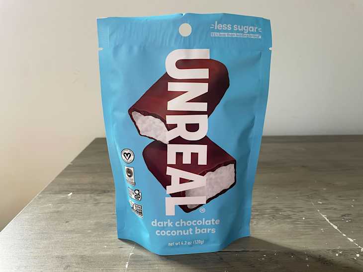 Packaging of Unreal dark chocolate coconut bars on a wooden surface, featuring a blue background and bold text.