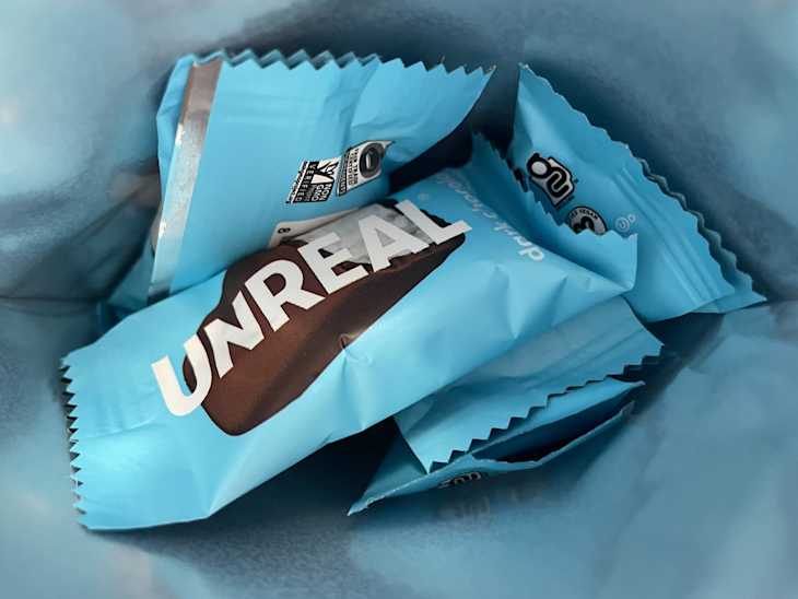 Several blue snack wrappers with "UNREAL" printed on them, partially visible in a light blue container.