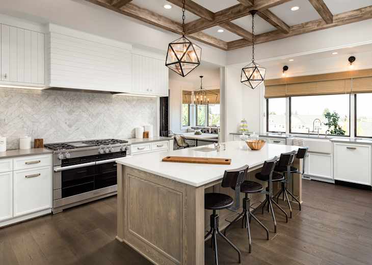 Kitchen Interior with Island, Sink, Cabinets, and Hardwood Floors in New Luxury Home. Features Elegant Pendant Light Fixtures, and Farmhouse Sink next to Window