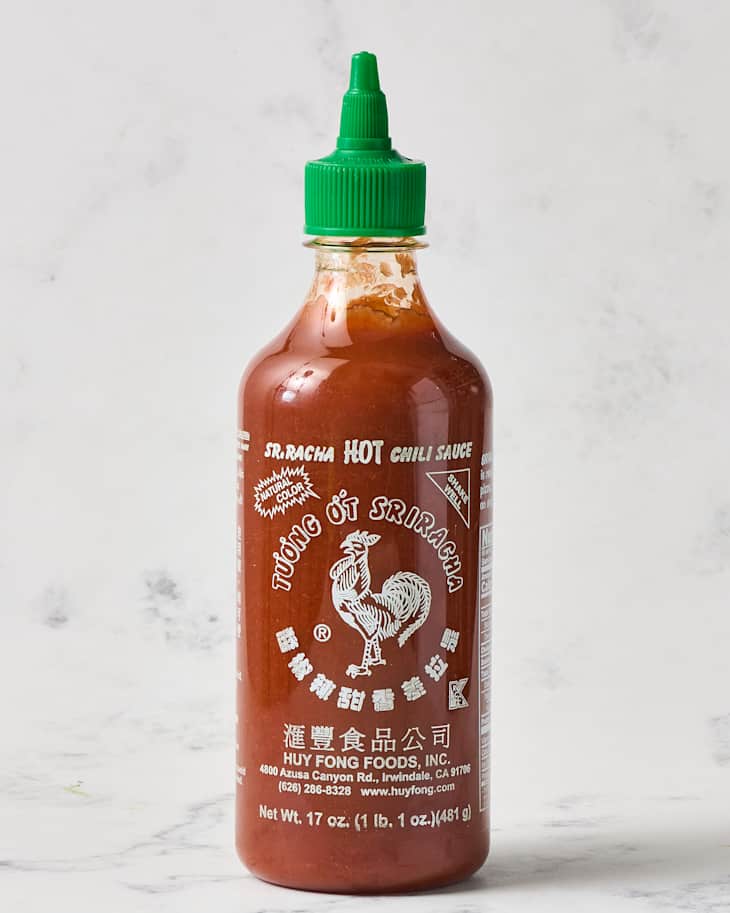 Huy Fong Sriracha hot chili sauce bottle with a green cap, featuring a rooster logo and white text on a marble background.