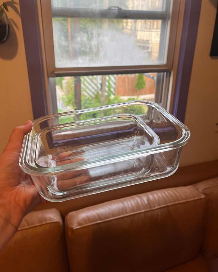 Clear glass baking dish held in hand, with a view of a window and brown couch in the background.
