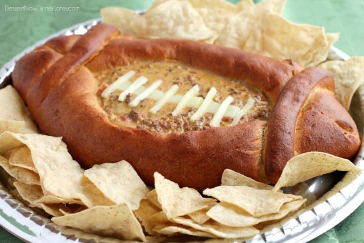 Football-shaped bread bowl with cheese dip and tortilla chips on a platter.