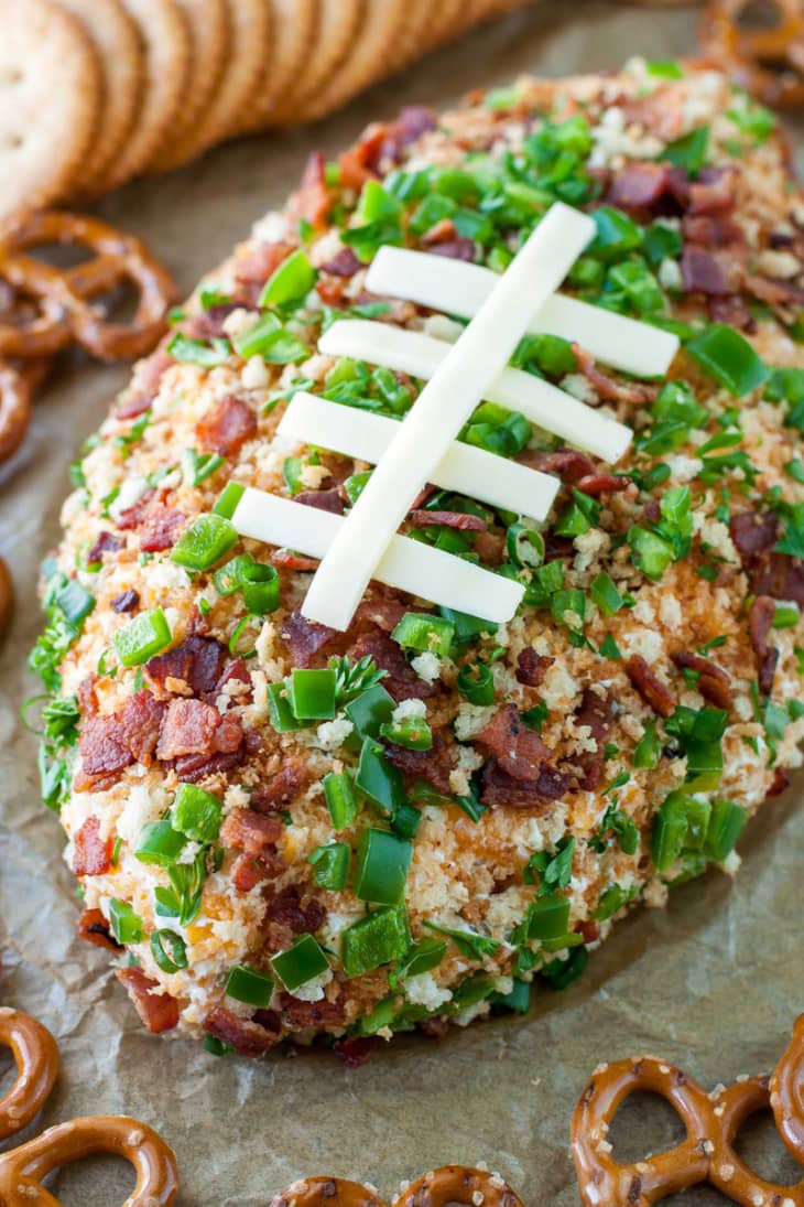 Football-shaped cheese ball with bacon, green onions, and pretzels, topped with cheese laces.