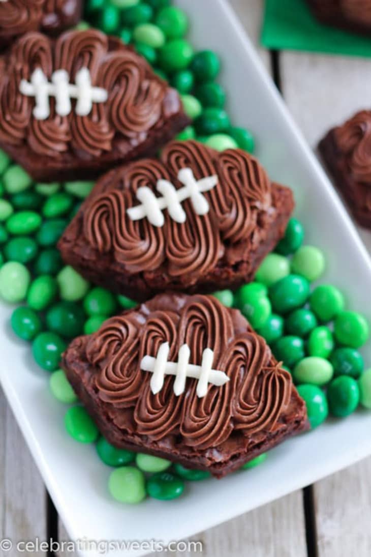 Football-shaped brownies with chocolate frosting laces on a bed of green candies.