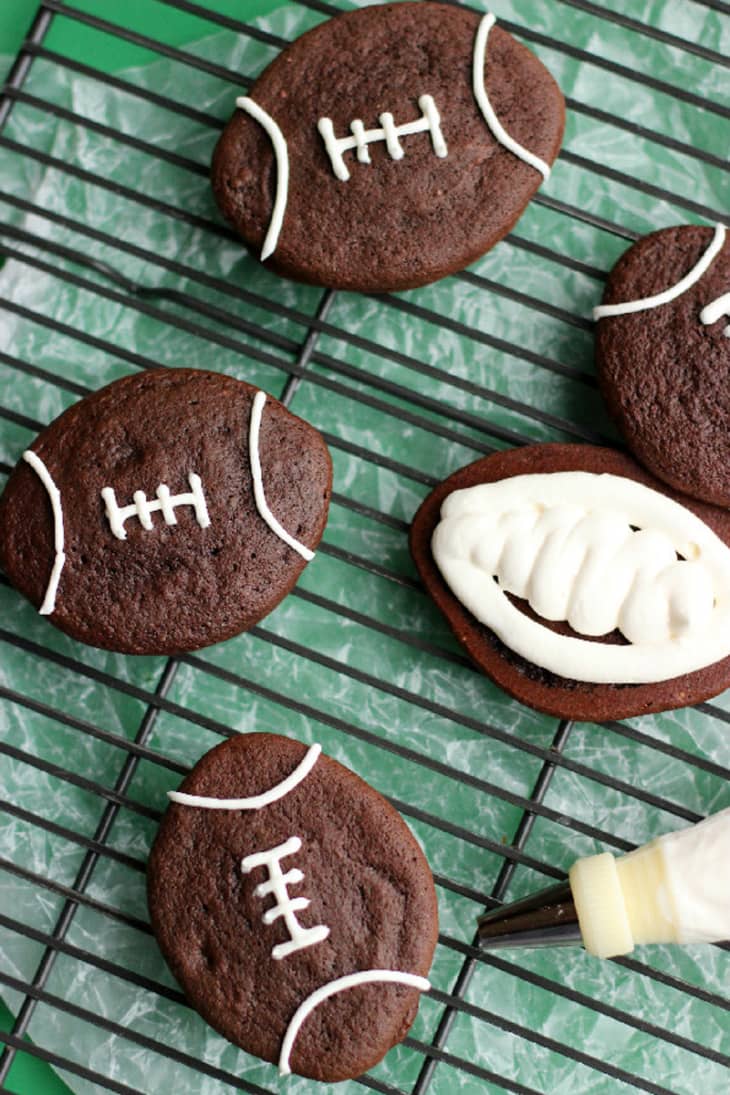 Football-shaped chocolate cookies with white icing details on a cooling rack.
