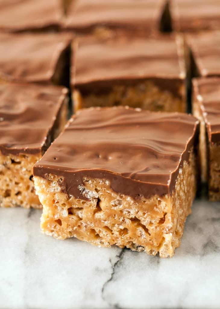Peanut butter rice krispie treats topped with a smooth chocolate layer on a marble surface.