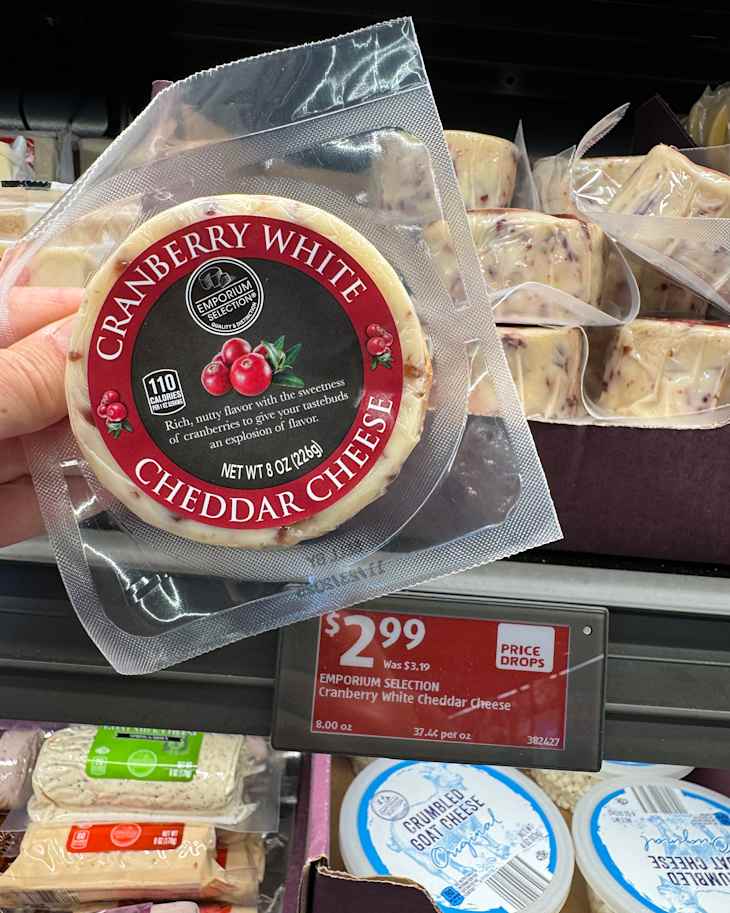 Cranberry white cheddar cheese in packaging held above a price tag showing $2.99, with other cheese products in the background.