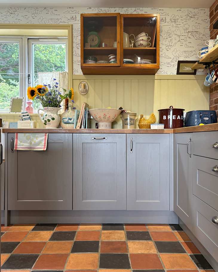 Cozy kitchen with gray cabinets, colorful tiled floor, vintage decor, and sunflowers in a vase.