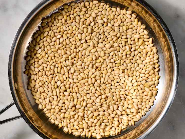 Pine nuts spread evenly in a stainless steel pan, showcasing their light beige color and smooth texture.