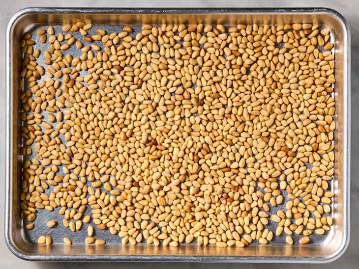 A metal baking tray filled with roasted pine nuts, showcasing their golden-brown color and varied shapes.