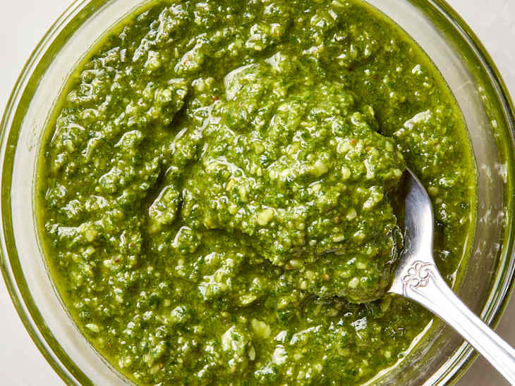 overhead shot of pesto in small glass bowl with a spoon in it.