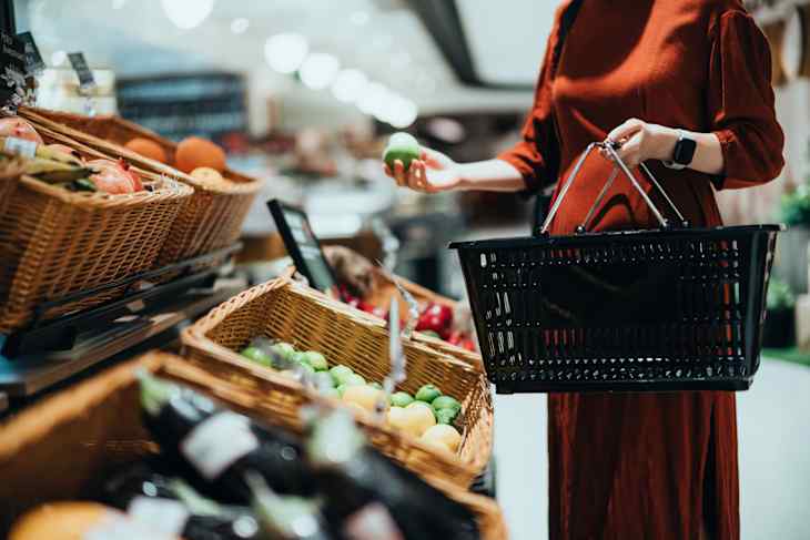 Woman carrying a shopping basket, grocery shopping for fresh organic fruits and vegetables in supermarket.