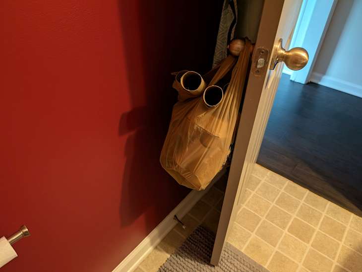 Toilet paper rolls in bag behind door.