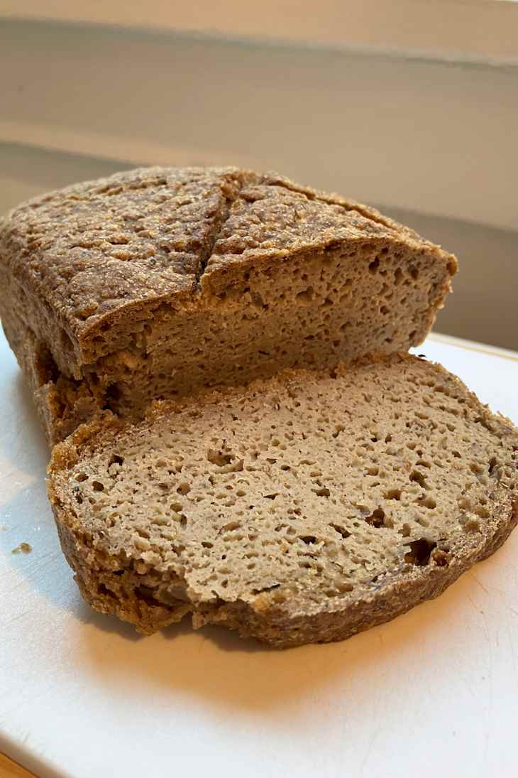 Sliced loaf of brown bread with a textured crust, revealing a soft, airy interior on a cutting board.