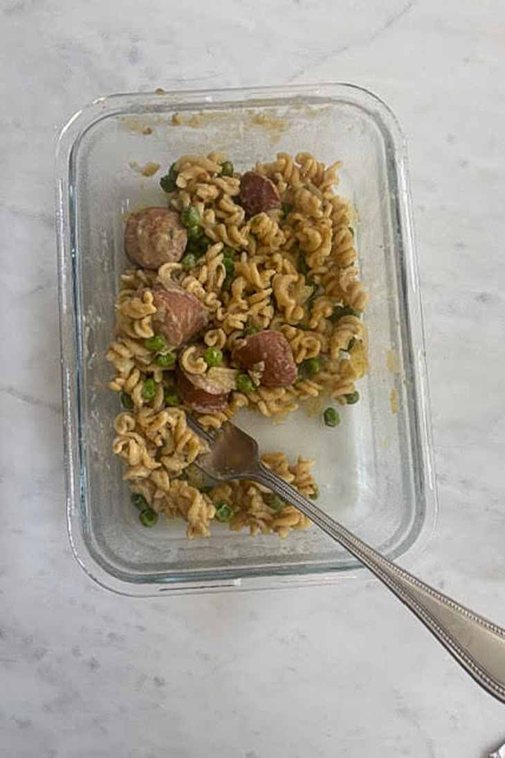 Pasta with sausage and green peas in a glass container.