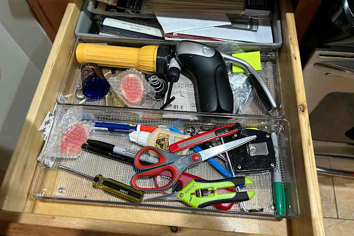 Messy kitchen drawer before decluttering using the 10 decluttering method.