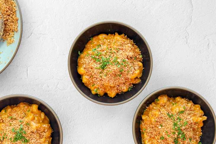 Creamy macaroni and cheese topped with breadcrumbs and parsley in a dark bowl.