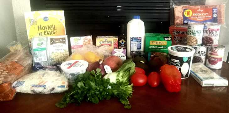 A variety of groceries including fruits, vegetables, dairy, canned beans, and rice products on a wooden table.