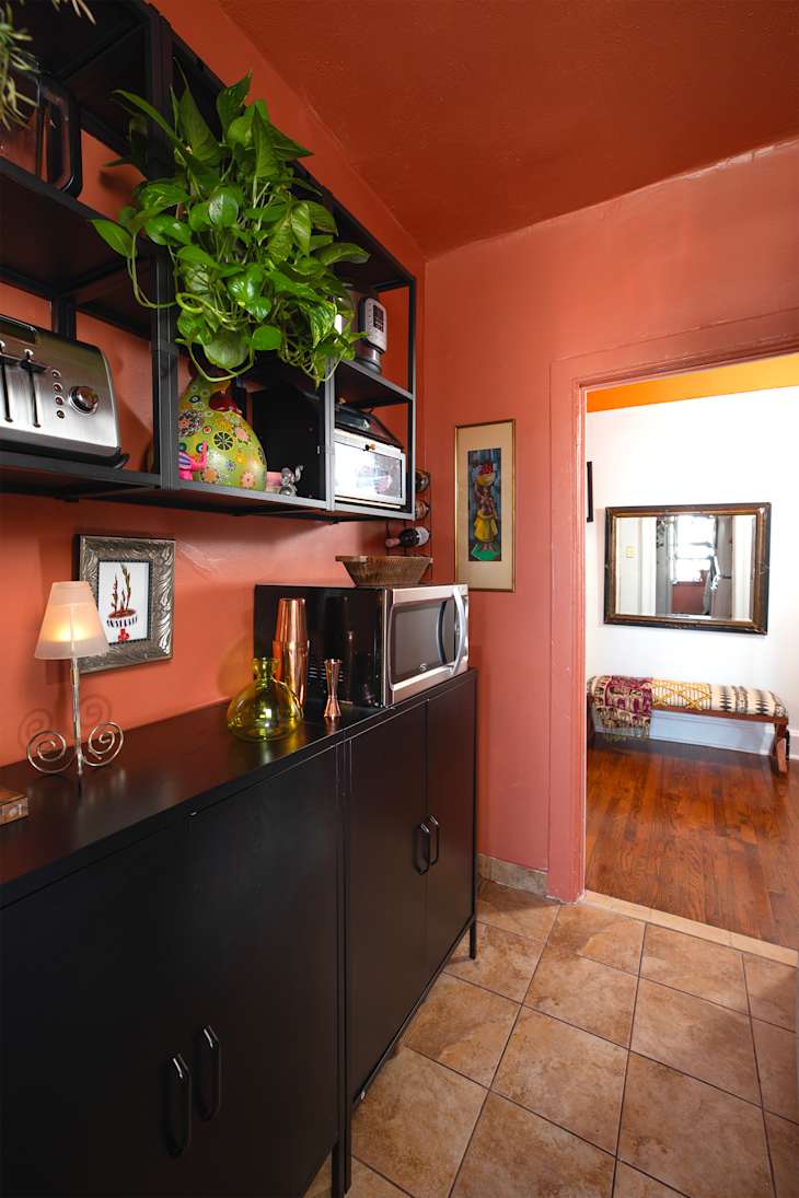 Cozy kitchen corner with black cabinets, a microwave, decorative plants, and colorful wall art.