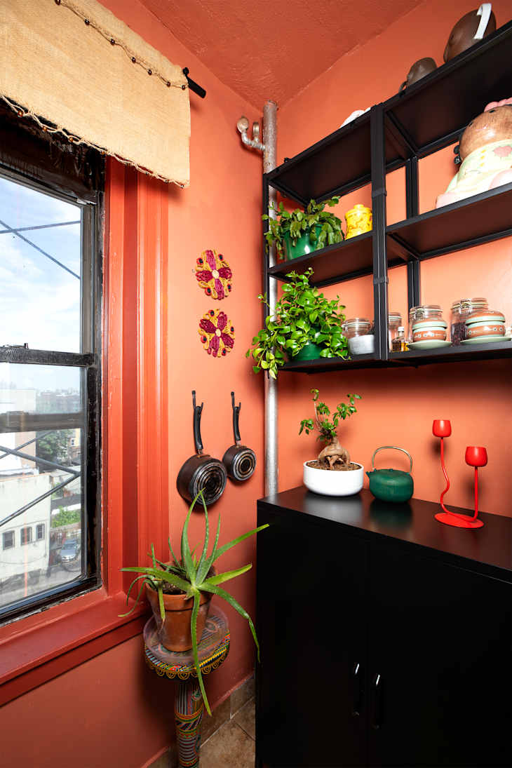 Cozy corner with orange walls, black shelving, potted plants, decorative candles, and vintage cookware.