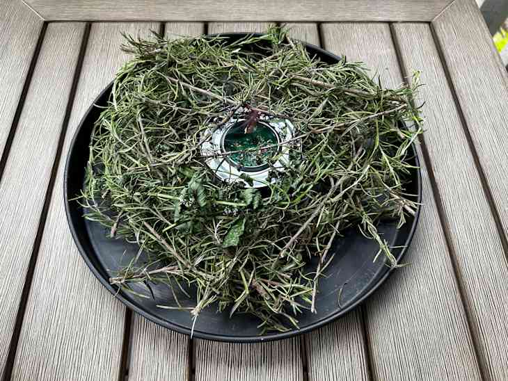 A plate of rosemary sprigs on a deck with a sterno can in the middle