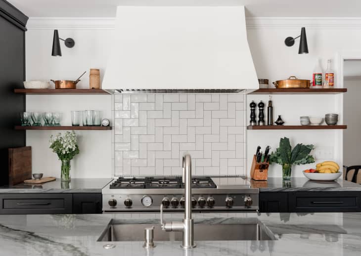 Modern kitchen with marble countertops, gas stove, white tile backsplash, open shelves, and stainless steel sink.