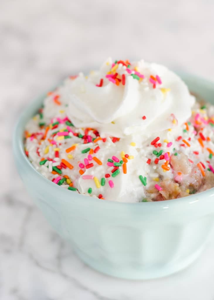 Whipped cream topped with colorful sprinkles in a light blue bowl on a marble surface.