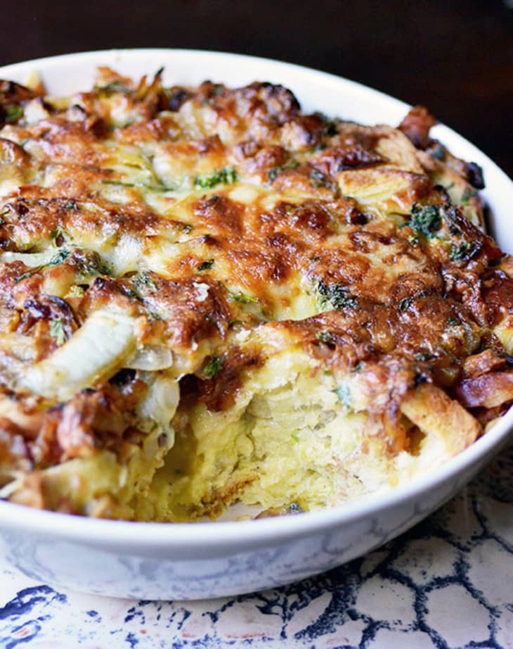 Cheesy broccoli and onion casserole in a white dish with a portion missing.