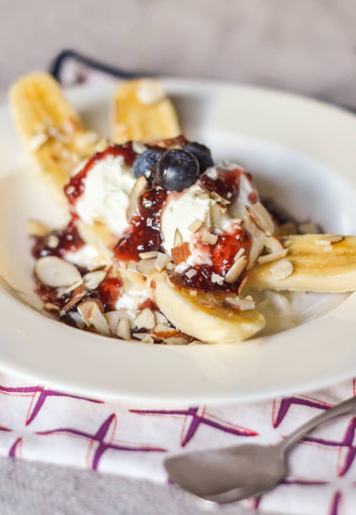 Banana split with yogurt, jam, sliced almonds, and blueberries on a white plate.