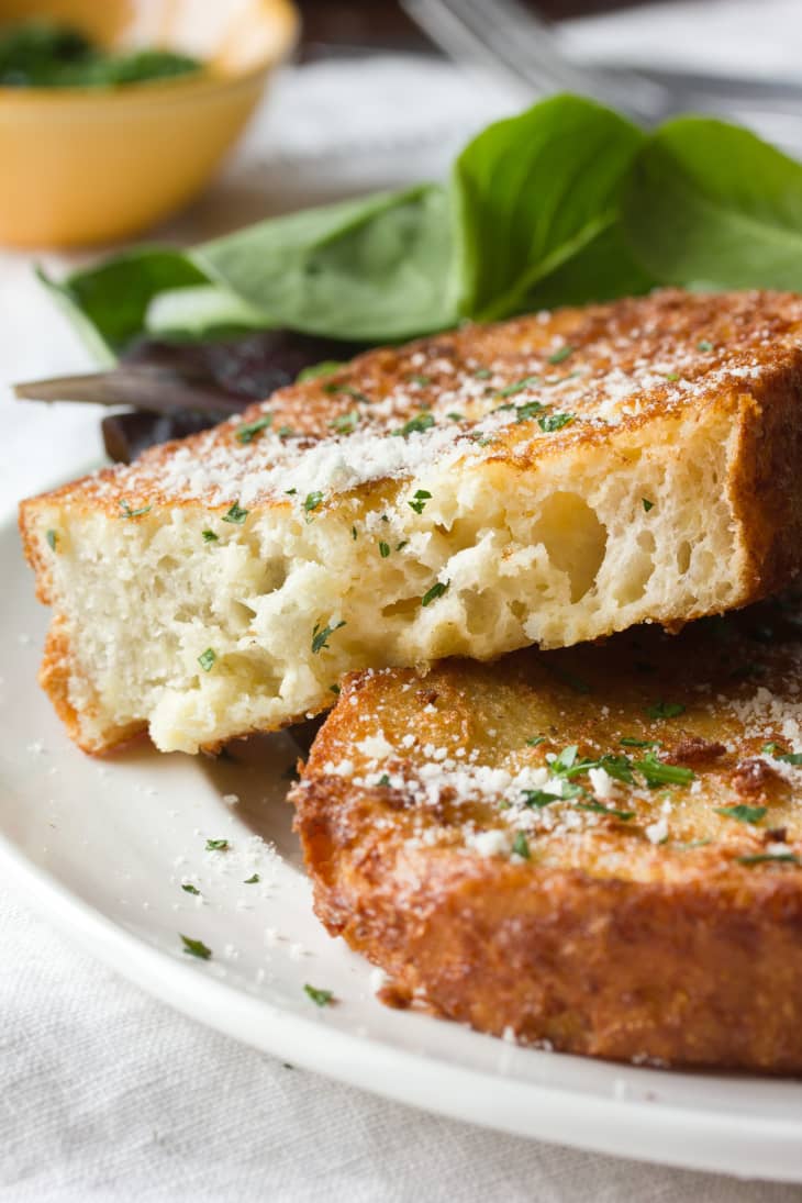 Thick slices of golden French toast topped with grated cheese and herbs on a white plate.