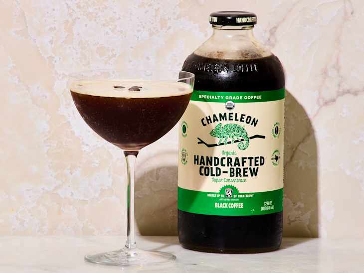 A glass of dark cold brew coffee garnished with coffee beans next to a bottle of Chameleon Organic Handcrafted Cold-Brew.