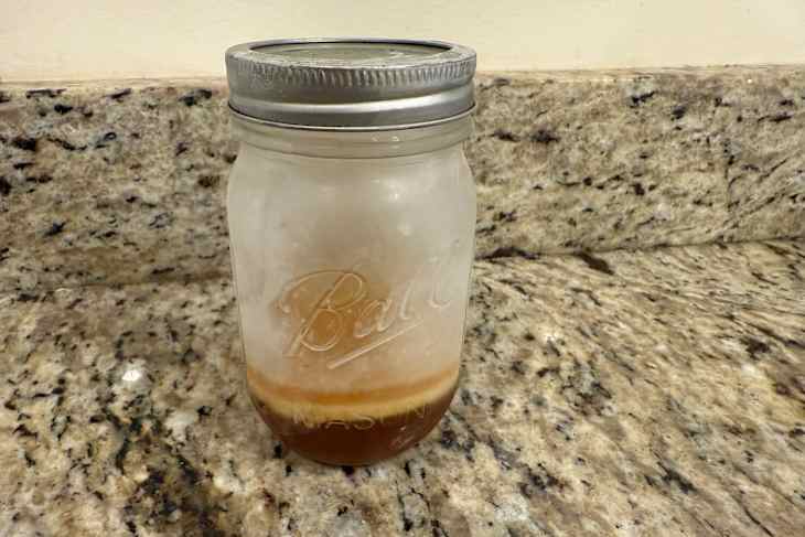 Frosted mason jar with layered liquid contents on a granite countertop.