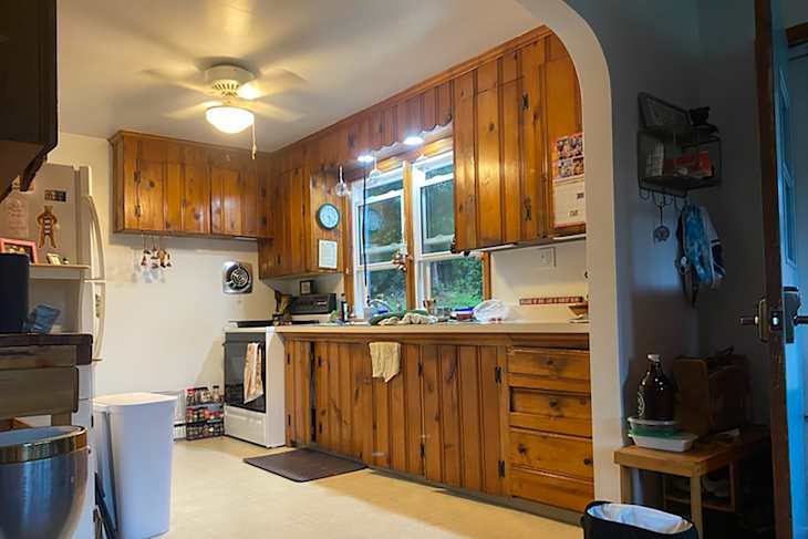 Cozy kitchen with wooden cabinets, white appliances, a ceiling fan, and a cluttered countertop.